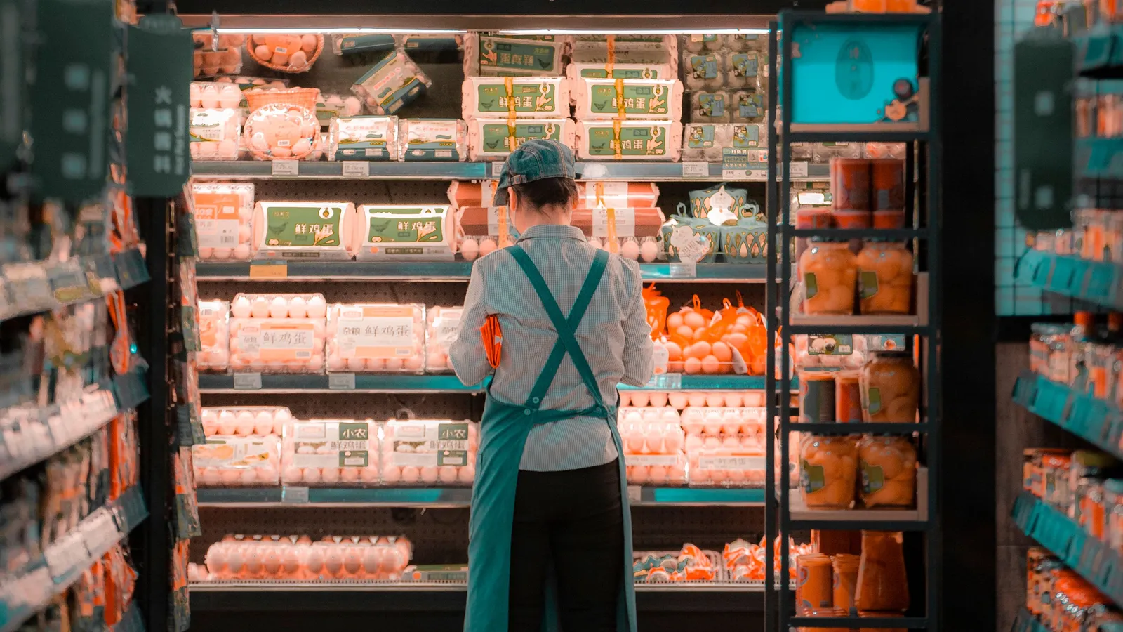Mitarbeiterin räumt Regale in einem Supermarktgang ein